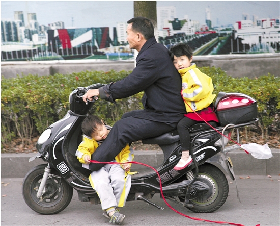 杭州下沙文渊路上，一名骑电动车男子带着两名小孩上路，让人为之捏了一把汗。 胡元勇 邹怡君 摄